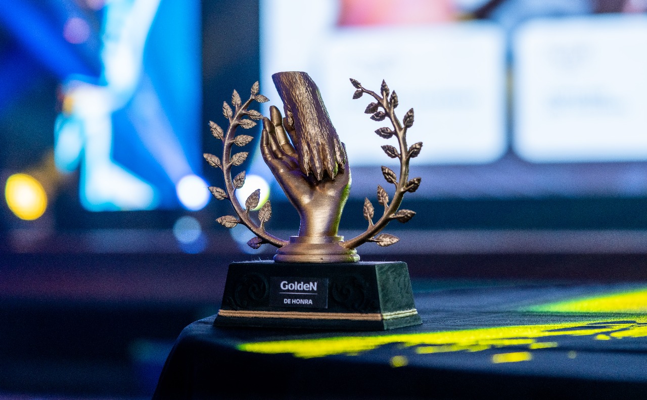 Troféu dourado produzido pela Axios Labs em ambiente de premiação com iluminação azul