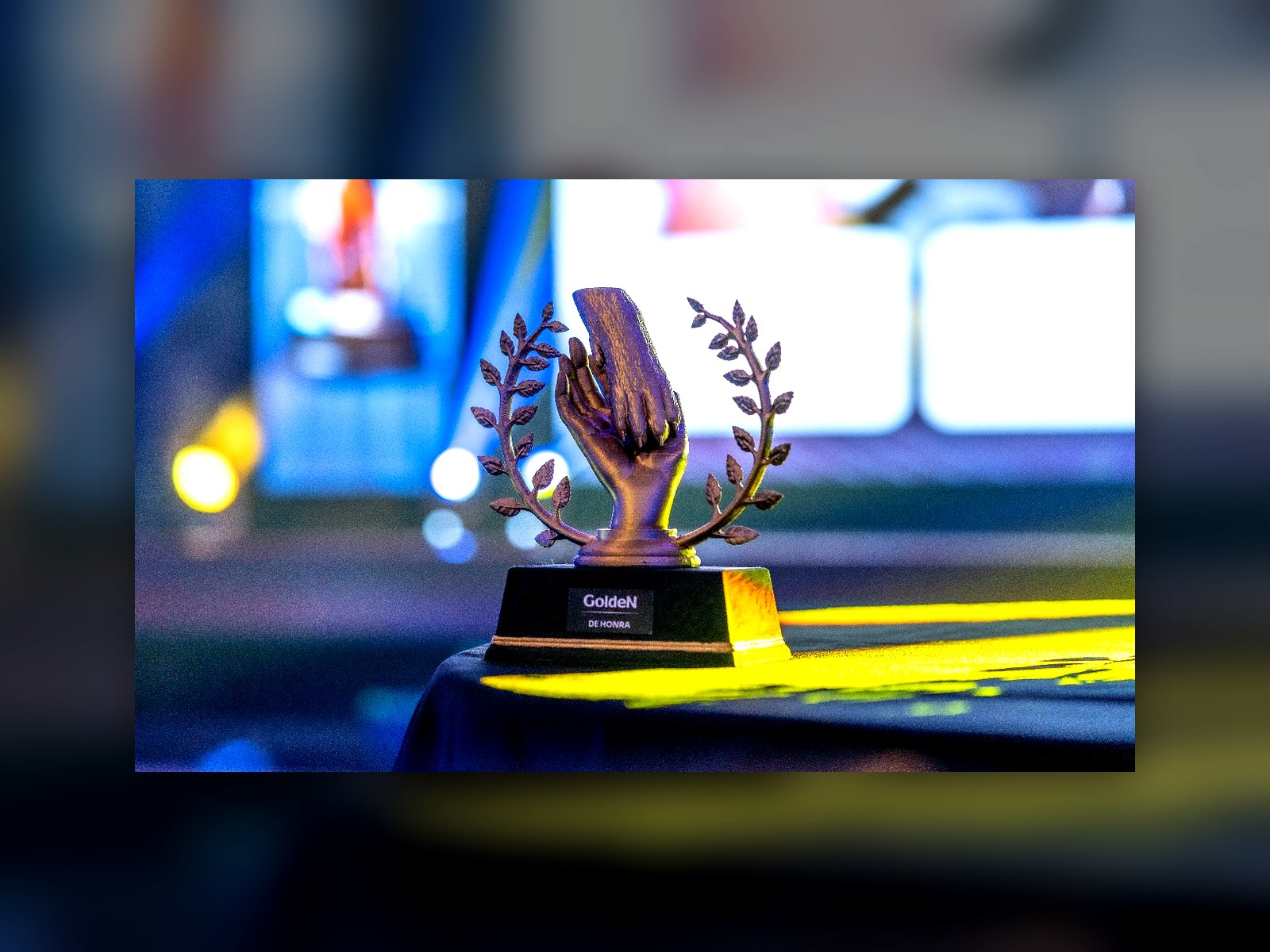 Troféu dourado com mãos e louros sobre base preta